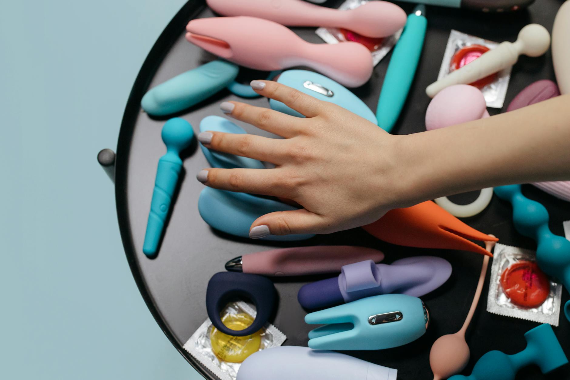 Two hands holding pink and blue silicone vibrators against a pastel background