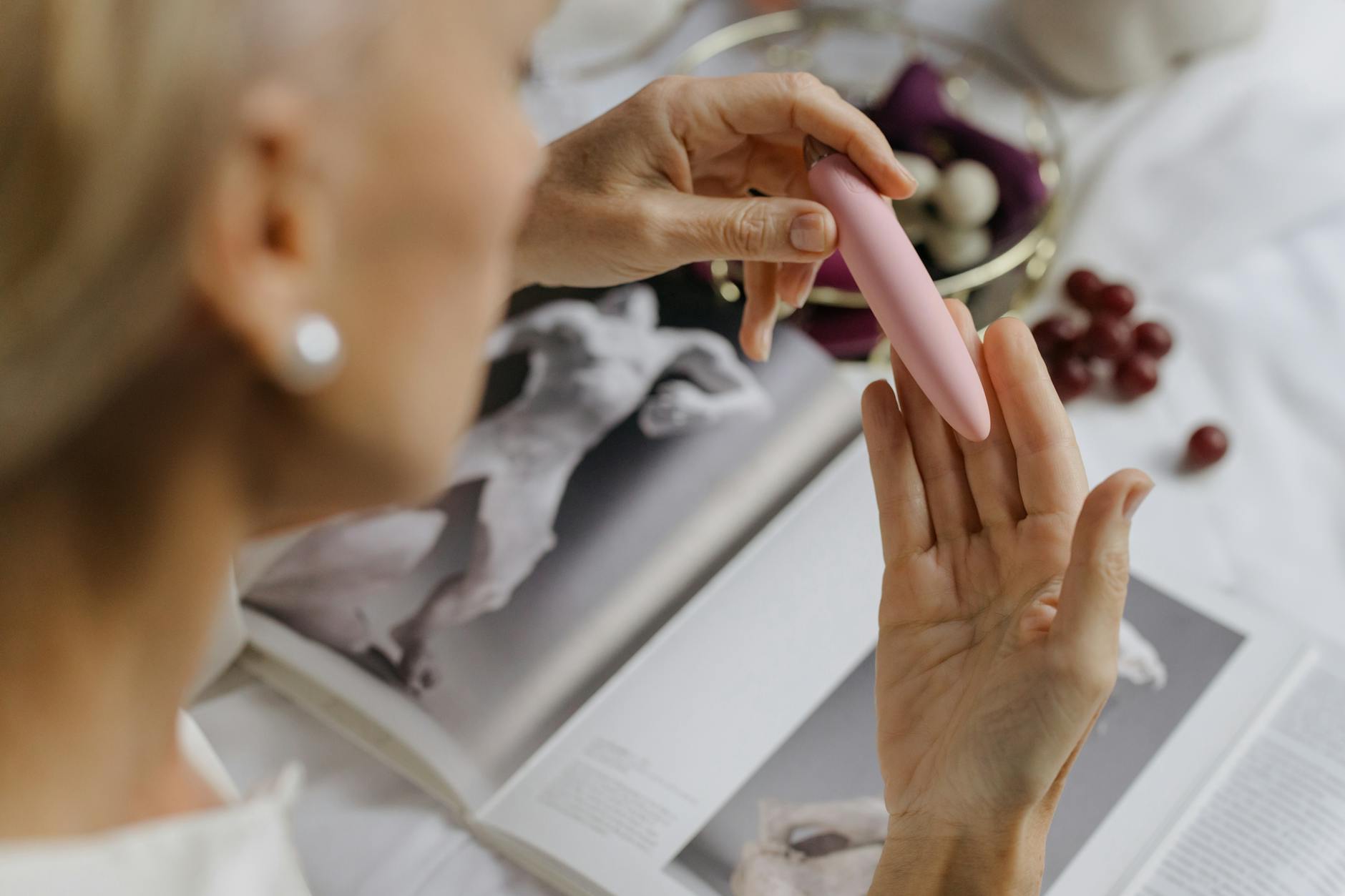 Close-up of a woman holding a pink silicone vibrator with books in background, emphasizing personal wellness