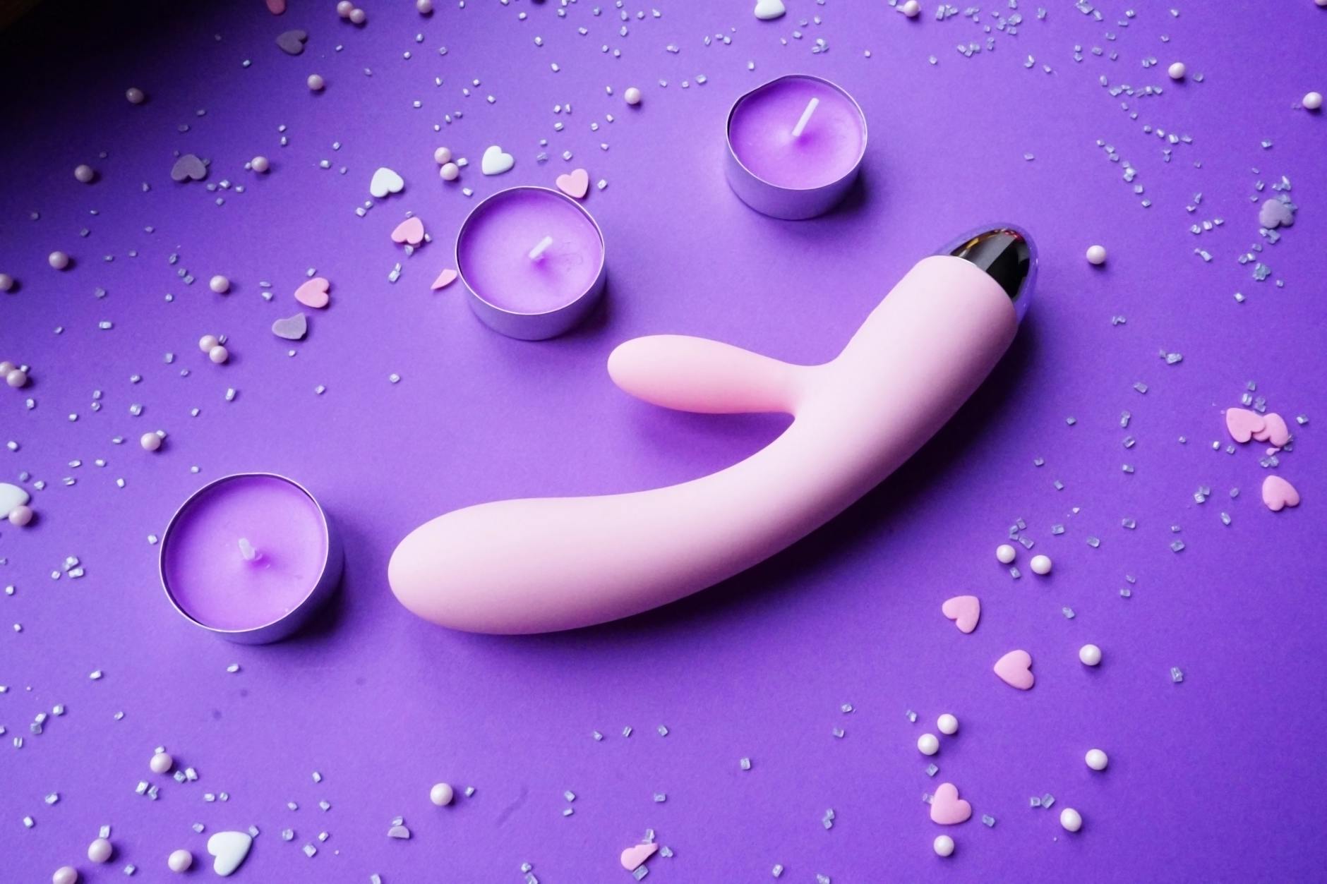 Pink clitoral vibrator on purple background with romantic candles and heart confetti